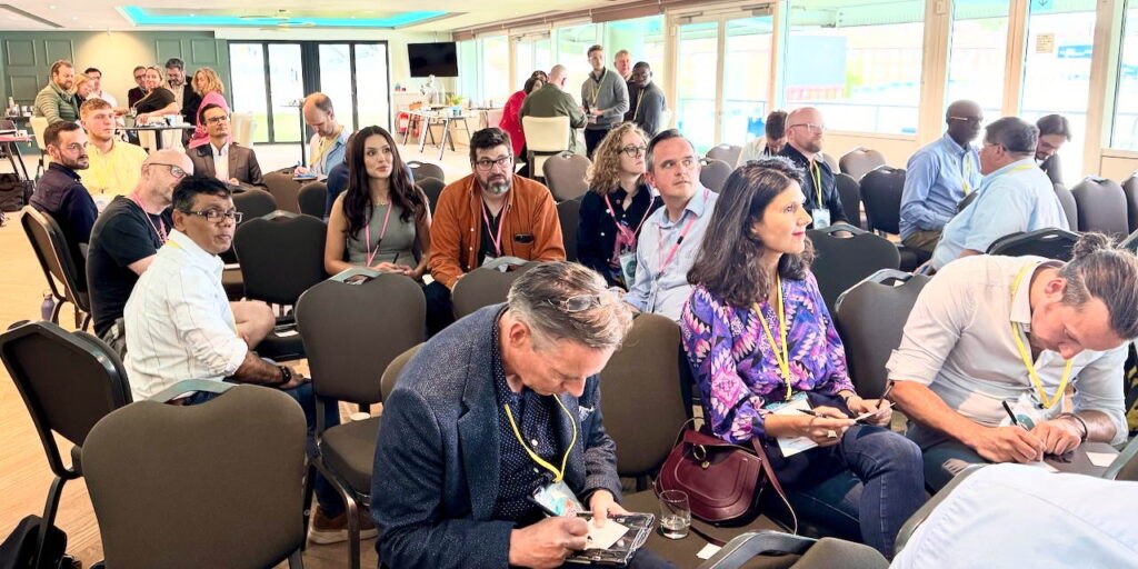 A diverse audience at an ASC conference sitting in informal, friendly groups, but focused on a presenter who is out of view.