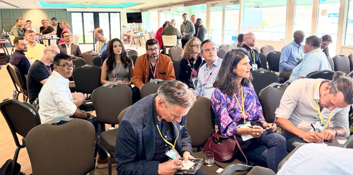 A diverse audience at an ASC conference sitting in informal, friendly groups, but focused on a presenter who is out of view.