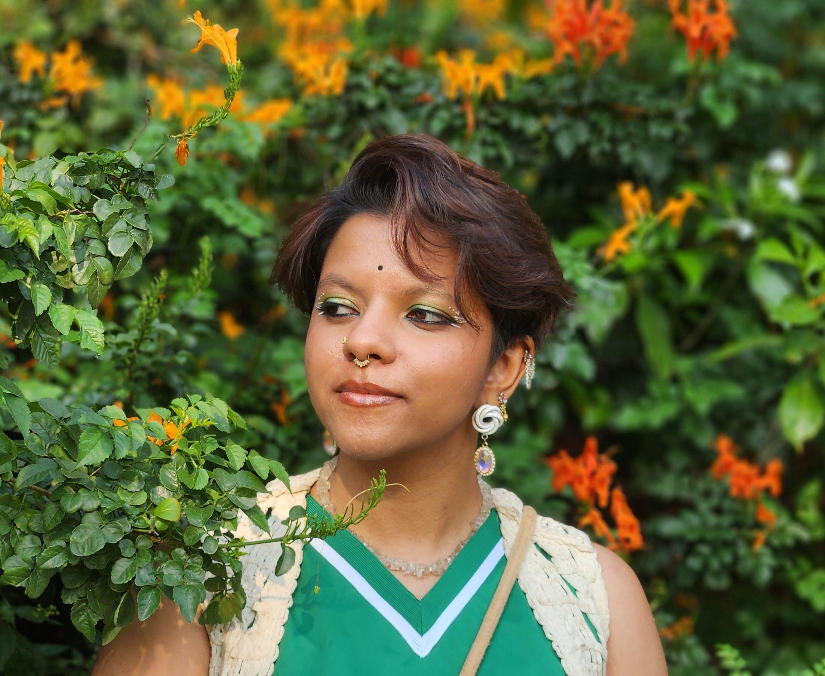 Photograph of Adhrushya Ganesh against a green flowering hedge of yellow and orange blooms. 